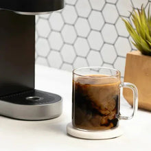 Glass mug filled with dark coffee on a countertop coffee machine base