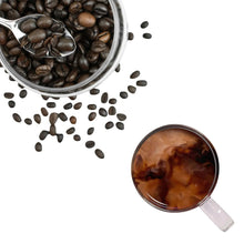 Roasted coffee beans in metal scoop with measuring cup of coffee