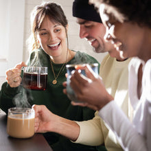 Two people holding mugs of coffee and cream on a table