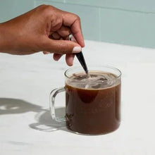 Person stirring instant coffee in clear glass mug