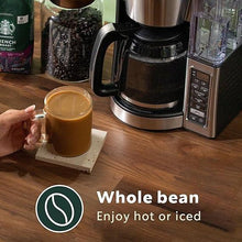 Whole bean coffee in glass cup with coffee maker on wooden counter
