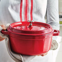 Red round Dutch oven with lid and side handles, held by two hands