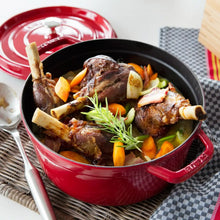 Red round Dutch oven with lid open, serving hot braised meat and vegetables inside