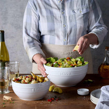 Staub white serving bowl set with salad, held by person in a blue button shirt