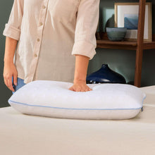 Latex cooling pillow on bed, white embossed cover with blue trim; person adjusts it