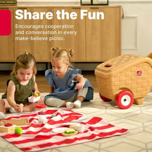 Toy picnic basket with red wheels next to children’s pretend picnic on striped mat