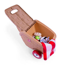 Open toy picnic basket with beige lid and wheels, holding pretend food and utensils