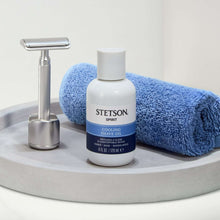 Cooling shave oil bottle on counter with metal razor and folded blue towel