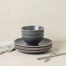 Gray stoneware dinnerware set with stacked bowls and plates on table