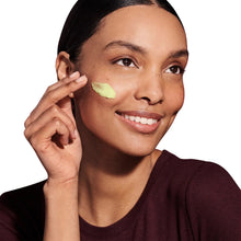 Woman applying retinol night moisturizer with green cream on cheek