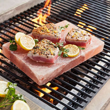 Himalayan salt block on grill with seasoned steaks and lemon halves