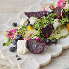 White marble platter with scalloped edges topped with beets, greens, and berries