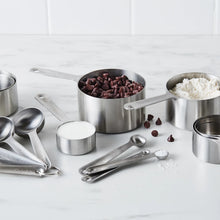 Stainless steel measuring cups and spoons set on countertop with dry ingredients