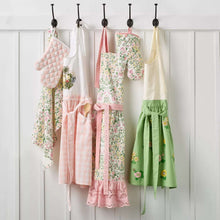 Hanging floral embroidered aprons in pink, green, and cream on hooks