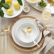 White dinner plate with thin gold rim, set with gold cutlery and napkin