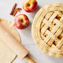 Wooden rolling pin with patterned dough sheet and open apple pie