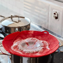 Red spill stopper lid with fan vent over a pot opening with steam