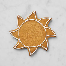 Sun-shaped cookie with white outline and carved details, brown gingerbread