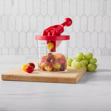 Tomato and grape slicer with red lid and handle, clear cup on wooden board with grapes
