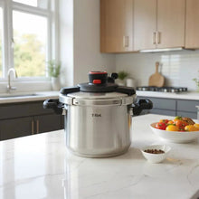 Stainless steel pressure cooker on stovetop with red control and black handles