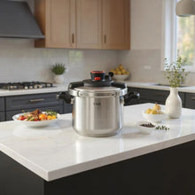 Stainless steel pressure cooker on stovetop with black lid base and red pressure knob