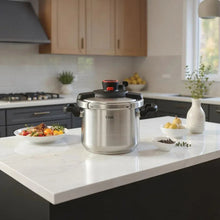 Stainless steel pressure cooker on kitchen counter with black side handles and red knob