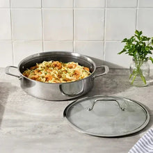 Stainless steel universal pan with side handles and lid set beside it on counter
