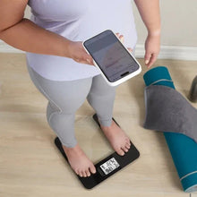 Body composition scale with digital display and glass platform, feet standing on it.