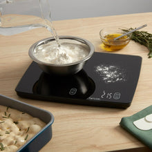 Black digital kitchen scale holding a bowl with flour and lit weight readout