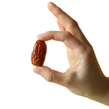 Pitted Deglet Noor dates held in a hand, dark reddish-brown and glossy