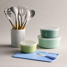 Blue cutting board with white-handled knife beside utensil tools in cups