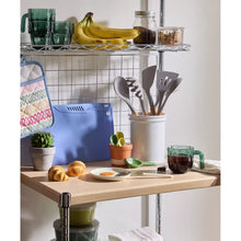 Blue cutting board on countertop with knife and hanging utensil tools