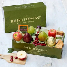 Green gourmet gift box open with fruit assortment and apple slice on wood board