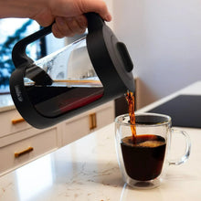 Black cold brew coffee maker pouring cold coffee into glass mug
