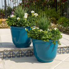 Two teal resin planter pots on patio steps with green foliage and white blooms