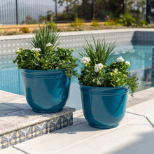 Two teal resin planter pots with rounded rim and white flowers