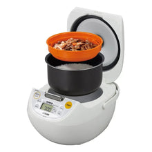 White rice cooker with open lid and orange serving bowl filled with food