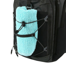 26-can backpack cooler side pocket with a bright blue towel secured by webbing