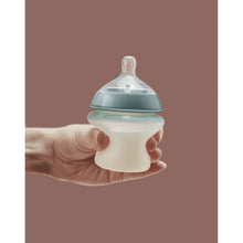 Tommee Tippee baby bottle held in hand, teal cap and white body with clear slow-flow nipple