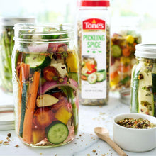 Pickling spice bottle beside jars of pickled vegetables and scattered spices