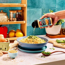 Hand holding spice bottle above rice bowl with green onion garnish