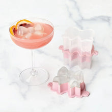 Bow-shaped ice cubes in pink silicone molds beside a drink glass