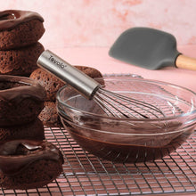 Stainless steel whisk in a glass bowl with chocolate batter beside brownies.