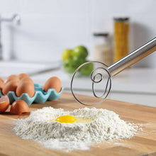 Stainless steel dough whisk lifting flour with an egg on a wooden countertop.