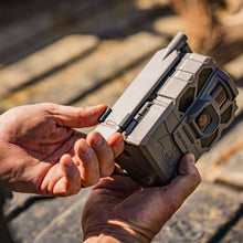 Trail camera in hands with side access panel open and internal components visible