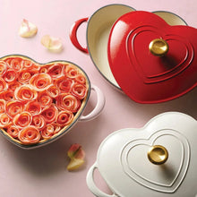 Heart-shaped dutch ovens in pink and red with gold knobs, lids partially off