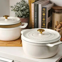 Two white enameled Dutch ovens with gold knobs and side handles