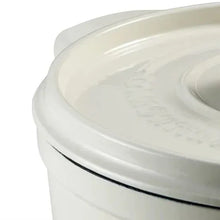 White enameled Dutch oven lid with raised oval pattern and gold knob, close-up