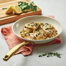 Cream ceramic fry pan with gold handle, filled with cooked food