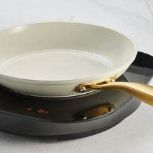 Cream fry pan on cooktop with gold handle, empty skillet